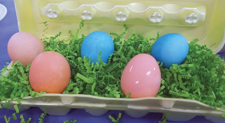Colored Easter eggs sitting on paper grass in an egg carton