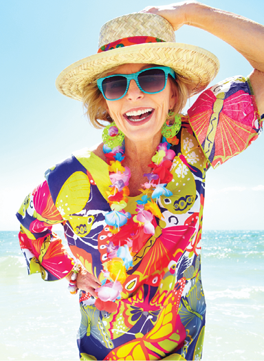 older adult woman dressed in vibrant summer blouse with summer hat sunglasses smiling at the beach