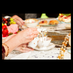 tea party setup with tea cup, fruits, and woman's hand serving tea